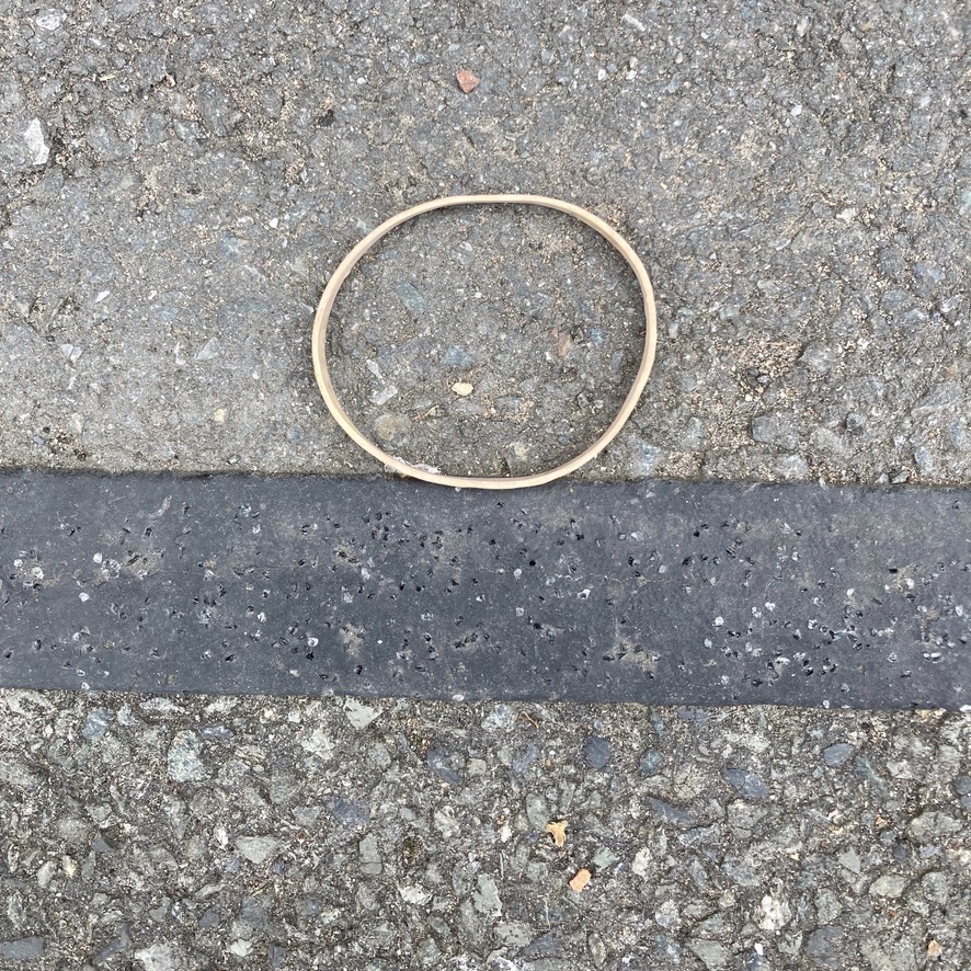 'Black Under Grey with Circle'. A discarded elastic band on a pavement. The pavement makes three broad stripes with the elastic band broadly circular in shape sitting atop a black stripe.