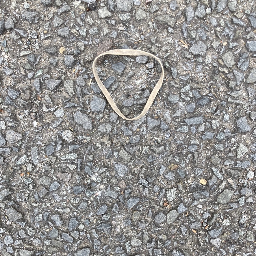 'Inverted Delta in Elastic' A discarded elastic band on the ground makes the shape of an inverted delta against the grey surface.