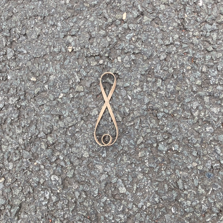 'I Made this shape for You'. A discarded elastic band on the ground makes a thin 'eight' shape. in the bottom section a added twist adds interest.