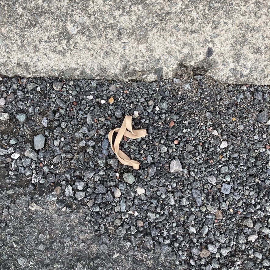 'Jump'. A discarded elastic band makes the shape of a dancer mid leap. The curb is light coloured and the jumping space is grey and stony.
