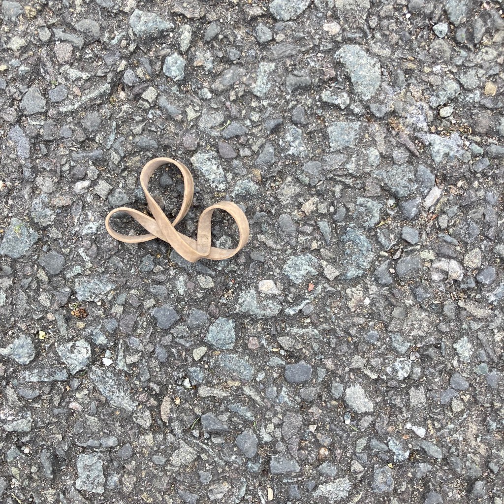 October on the #ElasticBandPhotos calendar features 'Variation on a Fleur de Lys'. A discarded elastic band on the pavement makes a twisted shape with three distinct loops.